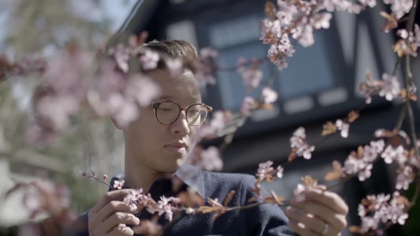 An asian man stands holding and looking at the branch of a cherry tree