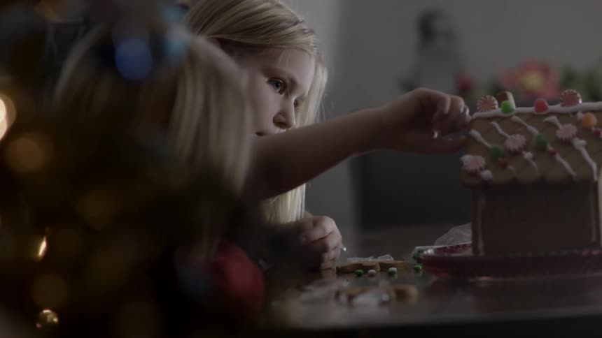Two young blonde girls admiring the gingerbread house in front of them on a table