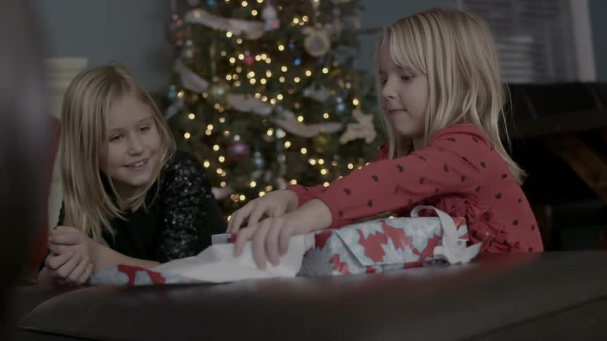 A little girl takes the wrapping off a christmas gift as family members watch