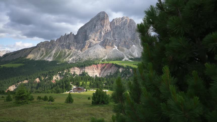 A house nested between the woods at the foot of the tall peaks of a mountain range
