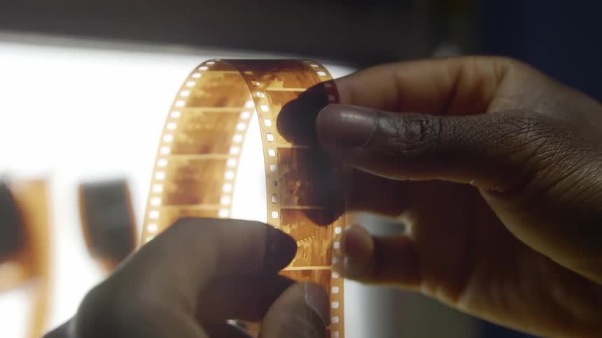 A piece of film is being held with hands in front of a light box indoors