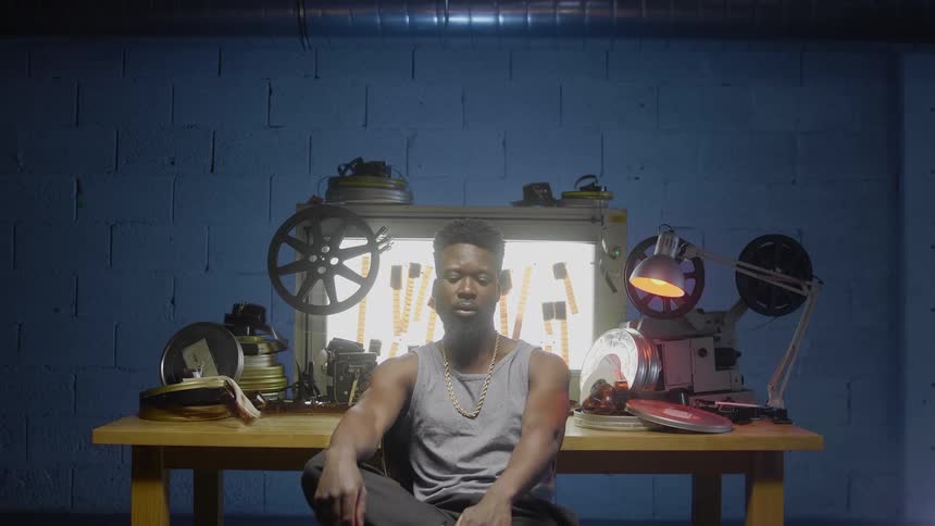 A man sits against a table with film and film equipment in a blue walled room