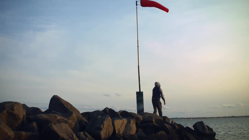 Man standing over the rocks in the coastline fly fishing under a cloth wind direction indicator