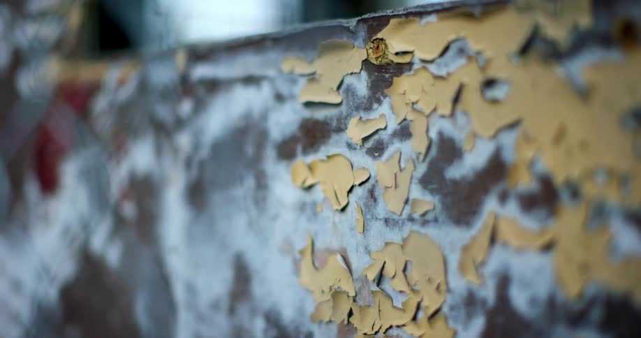 Yellow paint peeling off a wall with splotched white paint and a brown undercoat