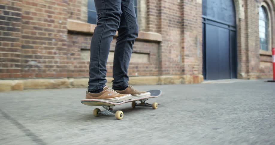 Man wearing pants and brown shoes skateboards in the street