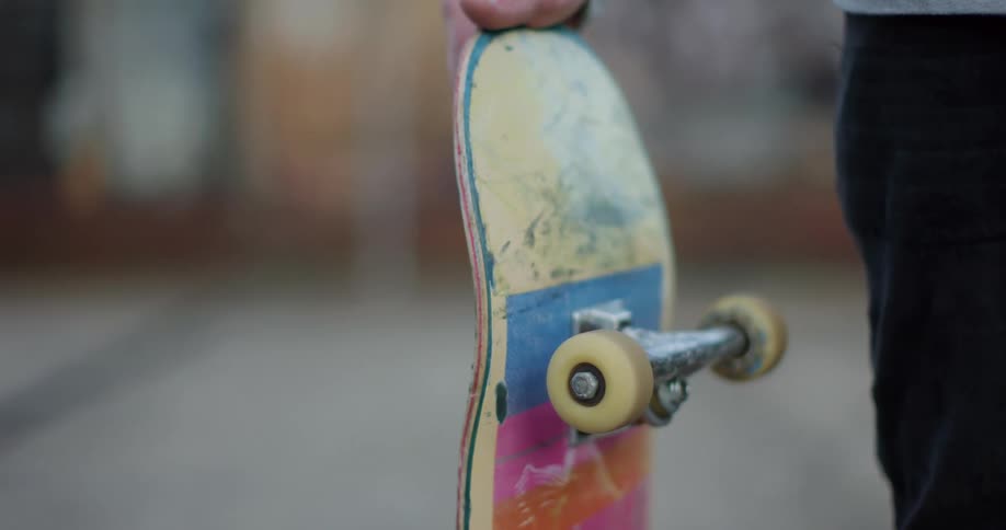 Man with black pants holds a skateboard with spinning small wheels