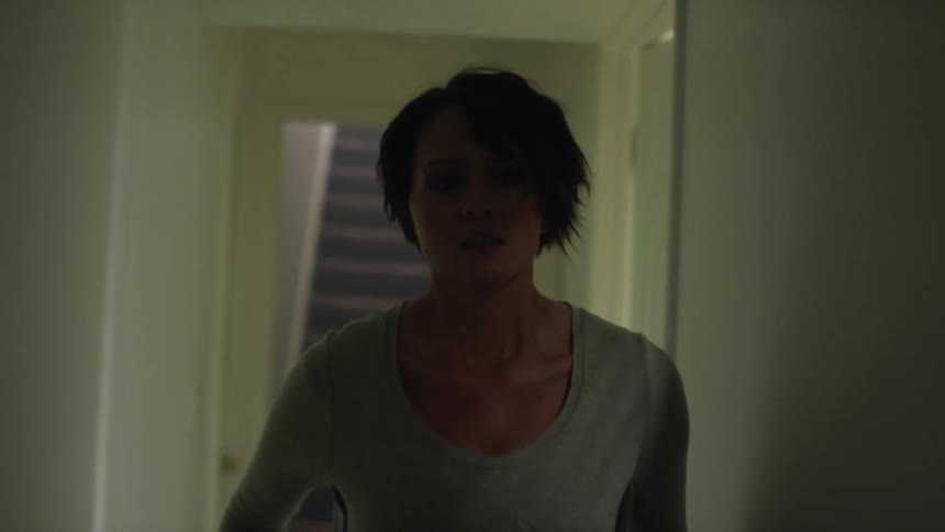 A woman walking down a hallway with doors with a staircase in the background