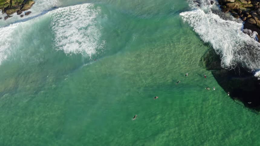 Aerial view of a coast and shoreline where people are swimming in the ocean down below at daytime