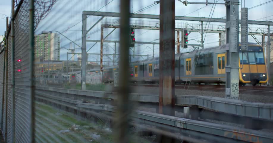 A train running on a train track with a fence in the foreground and the sky and clouds in the background