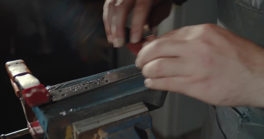 Mans hands rubbing a polishing brush across the surface of an unfinished knife on a machine