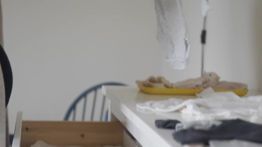 Woman opens a white dresser drawer and puts a baby onesie inside