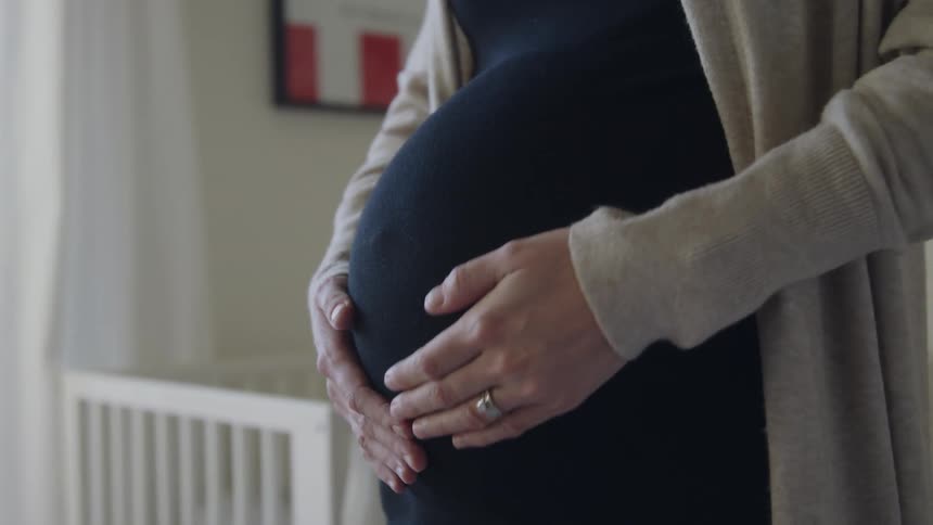 Young pregnant woman rubbing her belly in the babys room at home