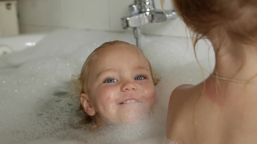Young blonde girls taking a bubble bath in a bathtub at home