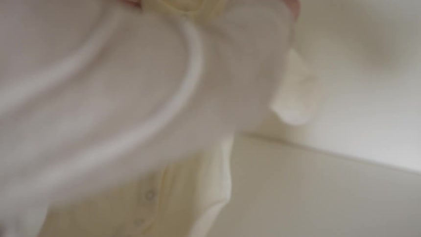 A person lifting a set of baby clothes on top of a dresser in a room at daytime