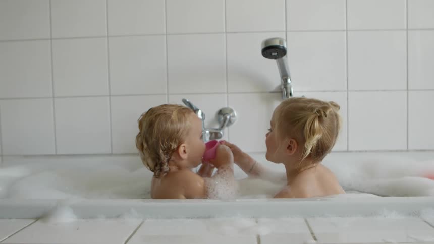 Little brother and big sister taking a bubble bath together and playing with toys inside a bath tub