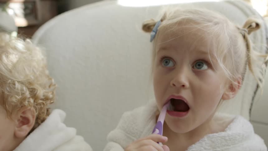 Two young blonde girls brushing teeth in a couch at home