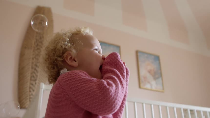 A young toddler girl plays with bubbles in her bedroom