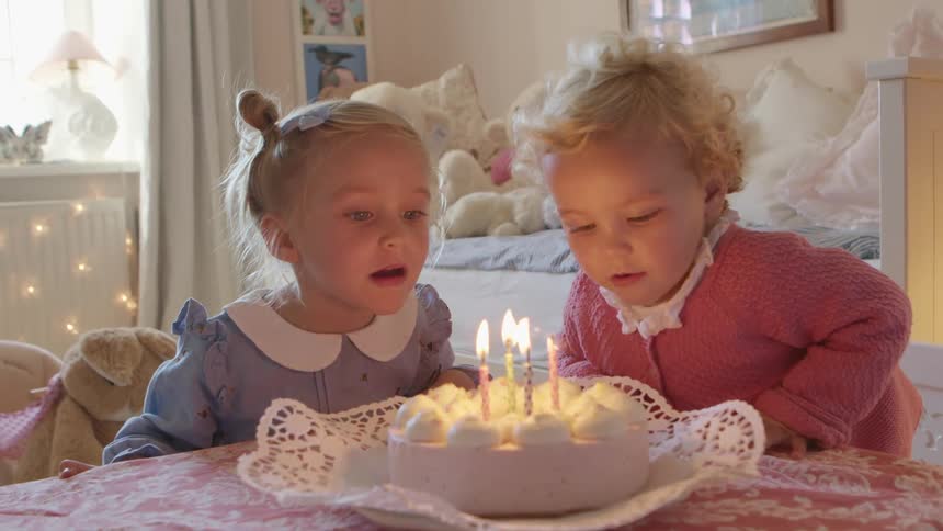 Baby girls blowing on the candles of a birthday cake in a room at home