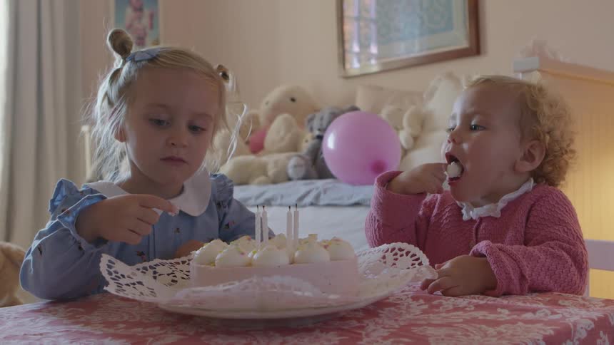 Little brother and big sister sitting at a small table in a childs room eating frosting off of a cake