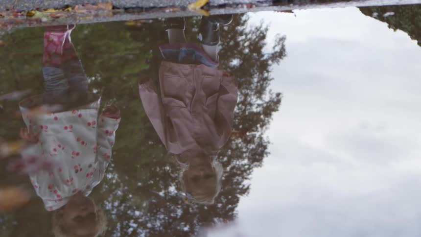 Little girl with a pink coat and black boots walks through a puddle