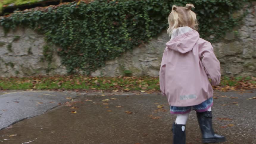 A blonde girl with pig tails runs in a circle on a puddle on pavement during the day