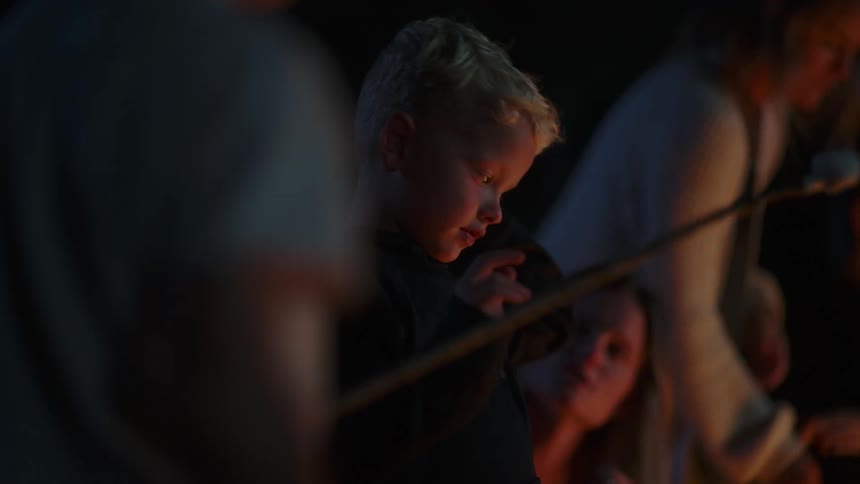 A young boy holding a stick with a marshmallow on it gets some pointers about cooking it over the fire