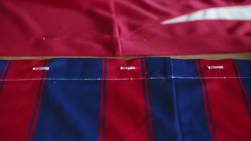 The hem of a red and blue sports jersey has white stitching across it