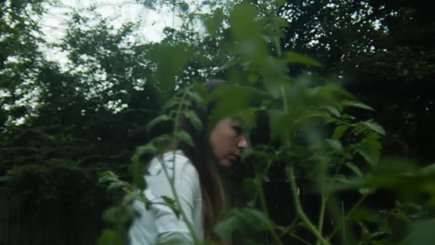 Woman with brown hair and a white shirt looks for something in the backyard