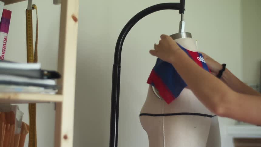 A woman pins fabric to the shoulders of a hanging dress form