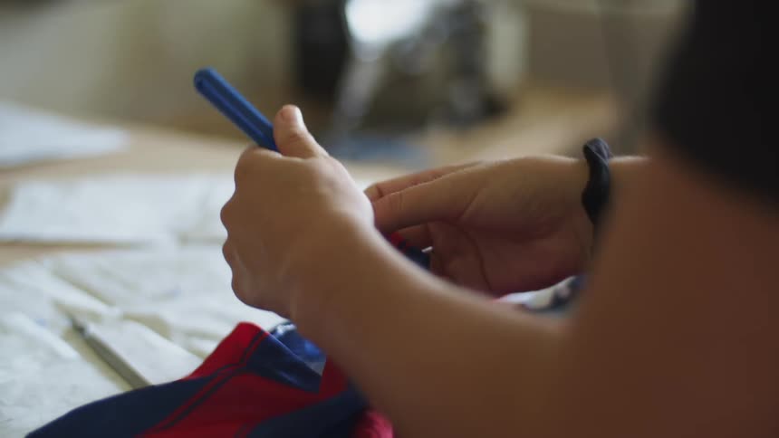 A woman stands at a table and uses a tool to rip the seam out of a red and blue fabric