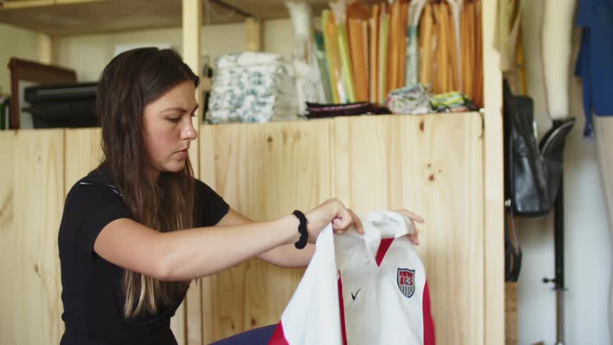 A woman crouches on the floor of a bedroom and thinks before folding a shirt