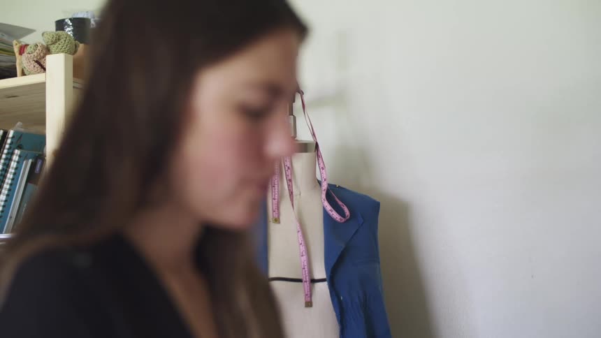A woman has her hand to her face concentrating while standing in front of a mannequin inside a room