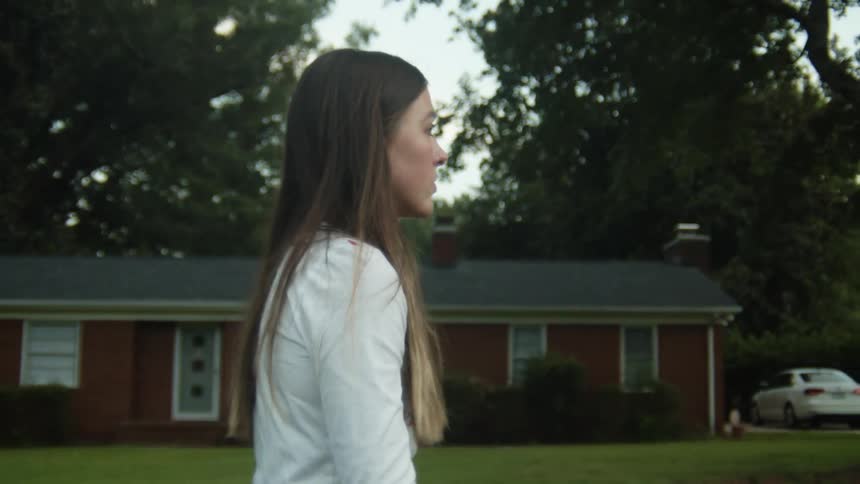 A woman walks in front of a neighborhood home by the road