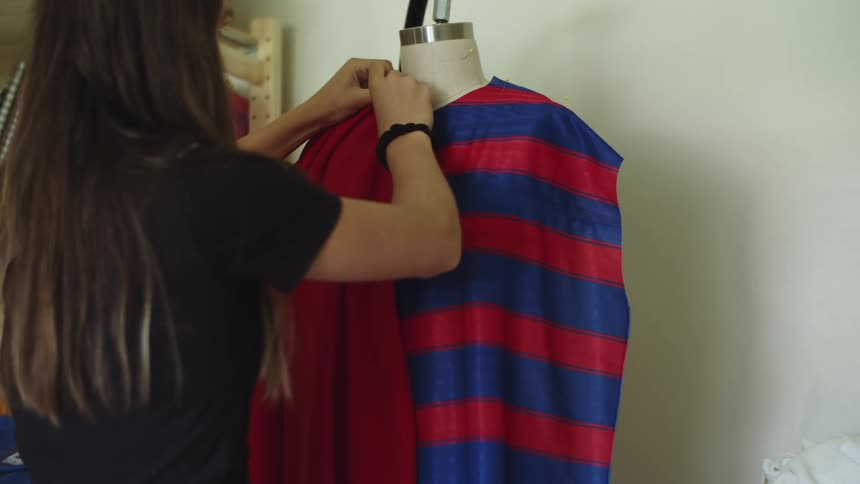 A woman tailoring a dress over a mannequin in her workshop at home