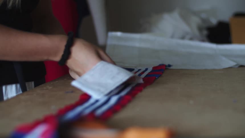 A woman unfolds a piece of white fabric while standing at a sewing table