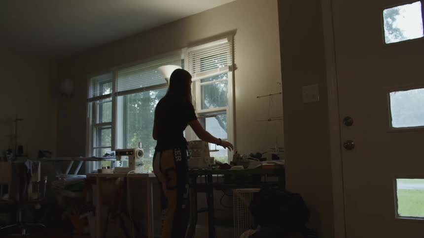 Woman walks over to a table inside of a home workshop with sewing supplies and picks up a spool