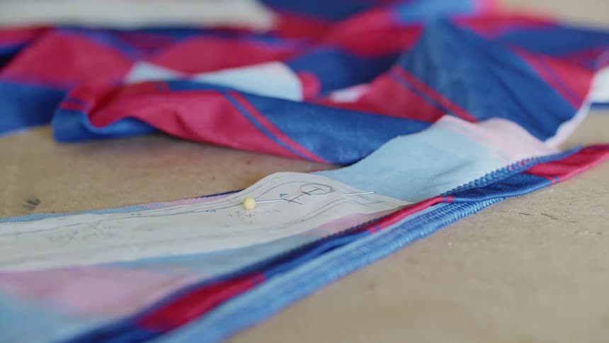Woman cutting a piece of blue and red fabric on a table with a pair of scissors