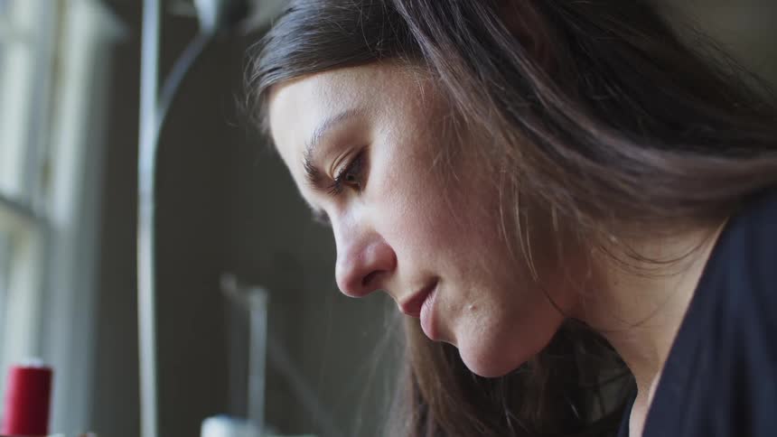 Woman looking down while sitting inside of a room in a house next to a window