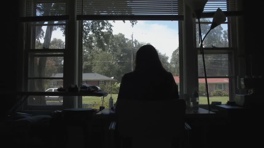 A woman sitting at a desk in front of a window at home