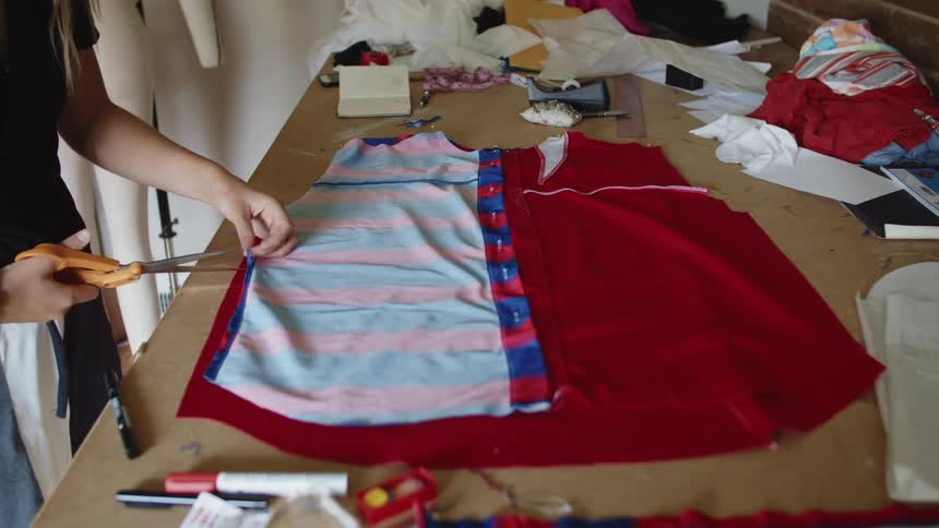 A woman lies fabric down on top of a shirt and cuts the fabric