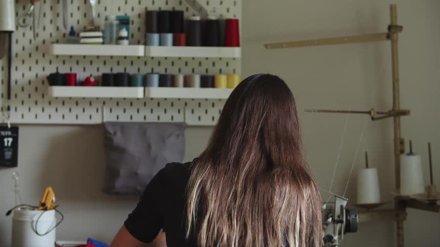 A woman sits at a table with sewing items surrounding her indoors