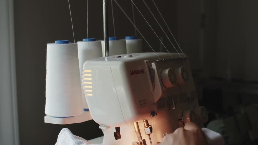 Woman using a sewing machine to stitch clothes in a dimly lit room at home