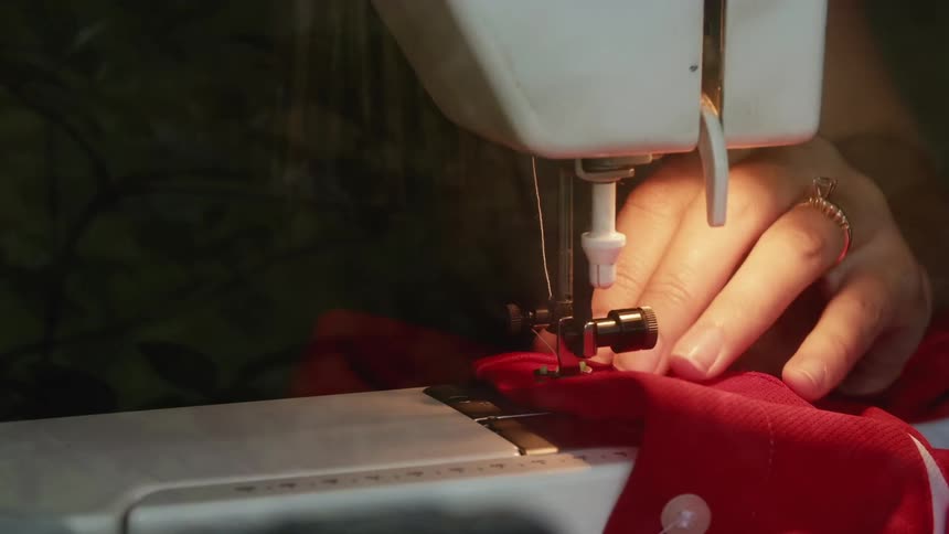 Womans hands using a sewing machine to sew a button onto a red shirt