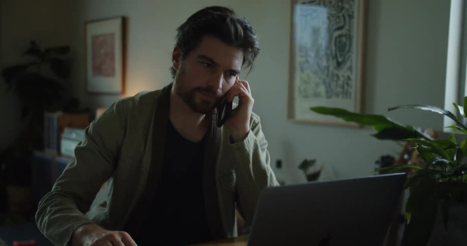 A bearded man is talking on his phone while looking through documents in a binder