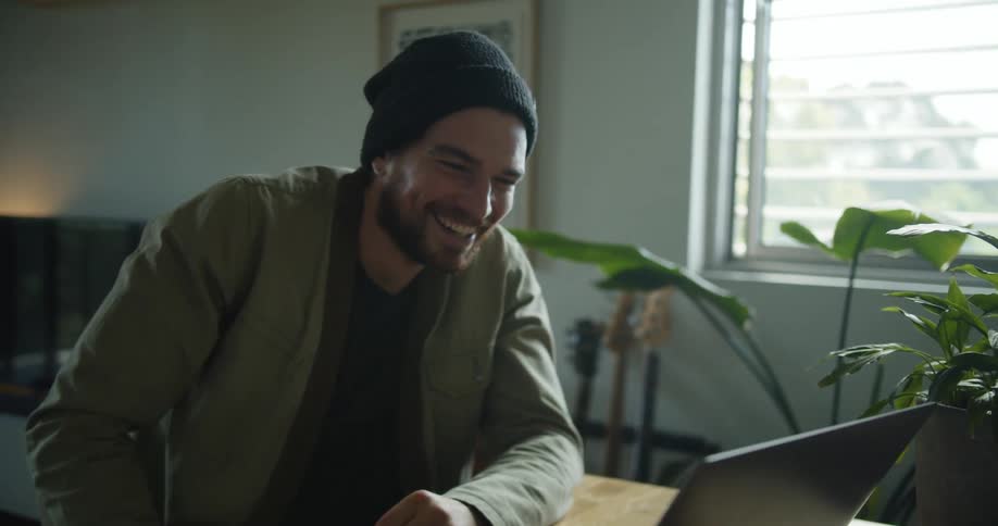 Man sitting at a desk in a home room video chatting on a laptop during the day