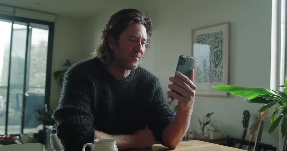 Man with long hair and a black pullover makes a video call on his iphone smartphone