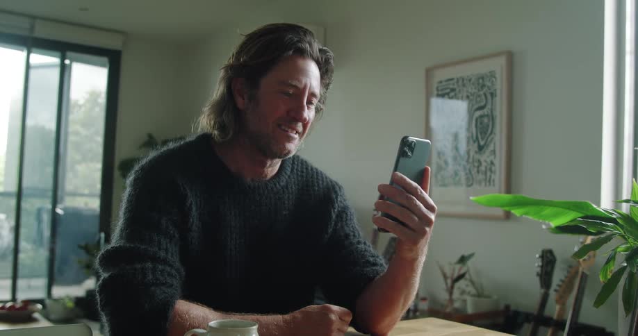 Man wearing a sweater says goodbye on a phone call at home