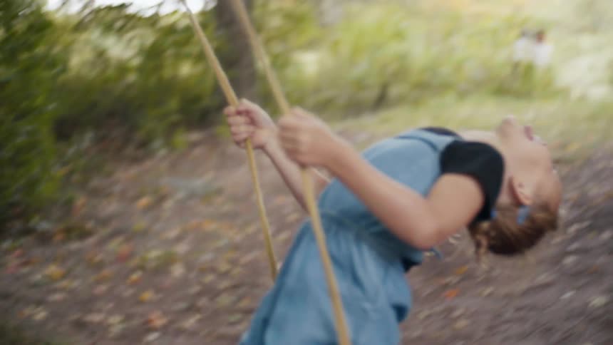Mother pushes daughter on a swing hanging from a tree outdoors