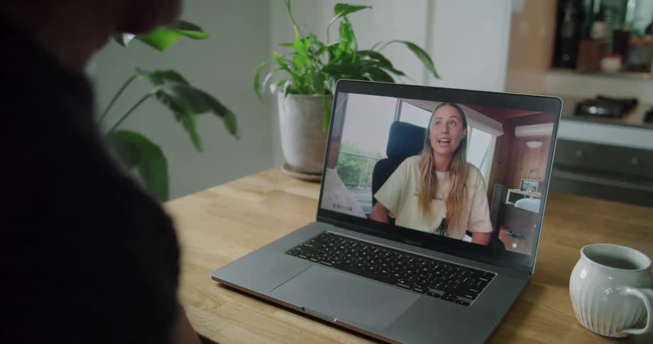A man sits at a table at home and video chats with a woman on his laptop