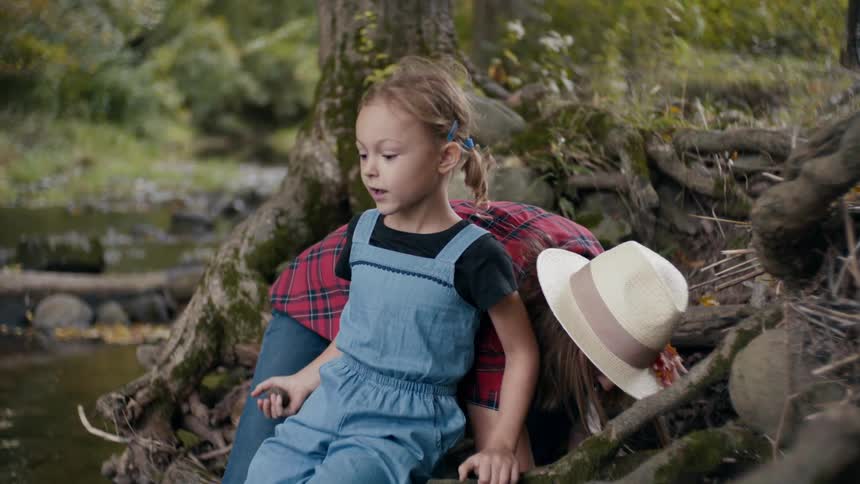 A woman bend down behind her daughter who is sitting on a tree in the forest during the day